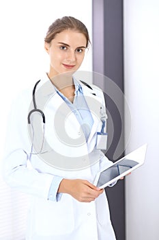Doctor woman in clinic office. Female physician at work using digital tablet while standing straight at hospita