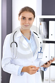 Doctor woman in clinic office. Female physician at work using digital tablet while standing straight at hospita