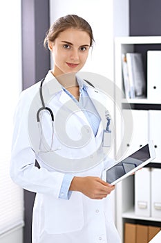 Doctor woman in clinic office. Female physician at work using digital tablet while standing straight at hospita