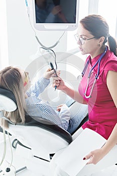 Doctor. Woman. Dentist talking to a young patient sitting on the dentist`s chair in the medical office. Shows in the