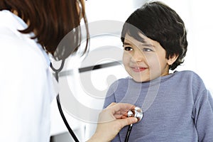 Doctor-woman examining a child patient by stethoscope. Cute arab boy at physician appointment. Medicine concept