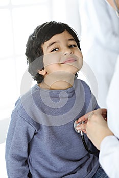 Doctor-woman examining a child patient by stethoscope. Cute arab boy at physician appointment. Medicine concept