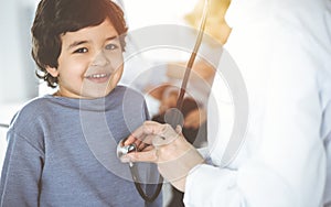 Doctor-woman examining a child patient by stethoscope in sunny clinik. Cute arab boy and his brother at physician