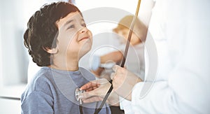 Doctor-woman examining a child patient by stethoscope in sunny clinik. Cute arab boy and his brother at physician