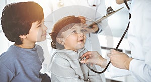 Doctor-woman examining a child patient by stethoscope in sunny clinik. Cute arab boy and his brother at physician