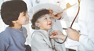 Doctor-woman examining a child patient by stethoscope in sunny clinik. Cute arab boy and his brother at physician