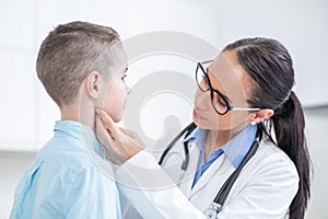 Doctor woman examining tonsils of young boy in medical office