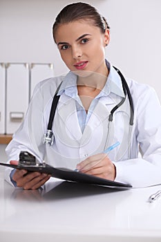 Doctor woman filling up medical form while sitting at the desk. Medicine and health care concept