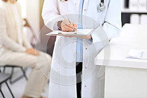 Doctor woman filling up medical form while standing near reception desk at clinic or emergency hospital. Unknown