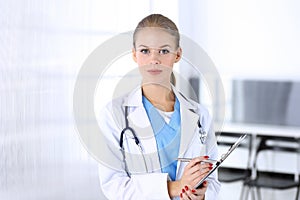 Doctor woman filling up medication history record while standing in emergency hospital office. Physician at work, studio