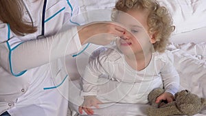 Doctor woman giving child patient remedy with spoon sitting with teddy bear