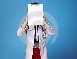 Doctor woman hoding clipboards front of face on blue