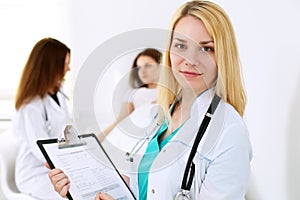 Doctor woman or nurse in a hospital office with her colleague and patient in the background. Healthcare and medicine