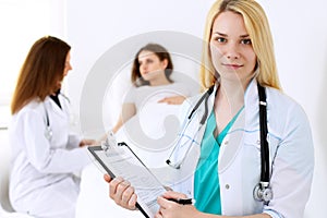 Doctor woman or nurse in a hospital office with her colleague and patient in the background. Healthcare and medicine