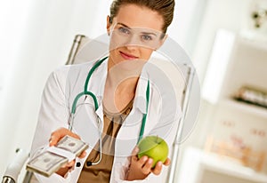 Doctor woman showing apple and pack of money