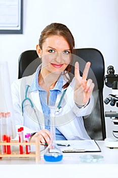 Doctor woman sitting at table and showing victory