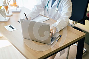 Doctor woman sitting and working on table using labtop and writing note at hospital