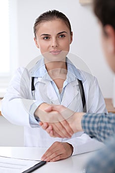 Doctor woman smiling while shaking hands with her male patient. Medicine and trust concept
