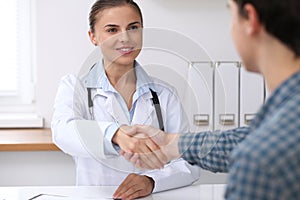 Doctor woman smiling while shaking hands with her male patient. Medicine and trust concept