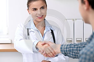 Doctor woman smiling while shaking hands with her male patient. Medicine and trust concept