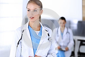 Doctor woman standing in emergency hospital office with colleague at background. Physician at work, studio portrait