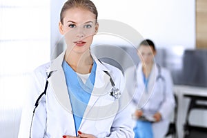 Doctor woman standing in emergency hospital office with colleague at background. Physician at work, studio portrait