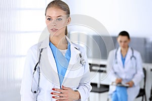 Doctor woman standing in emergency hospital office with colleague at background. Physician at work, studio portrait