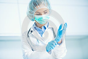 Doctor woman surgeon specialist in sterile clothing putting on surgical gloves