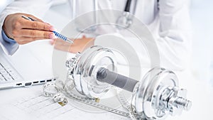 A doctor woman in surgeries prescribes sport movement and weight loss using dumbbells and a measuring tape