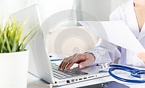 Doctor woman typing information of patient prescription from paperwork medical history form into laptop