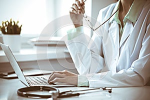 Doctor woman using laptop computer while sitting at the desk near window in hospital. Medicine and health care concept