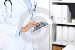 Doctor woman using tablet in clinic office. Unknown female physician at work while standing straight at hospital, close
