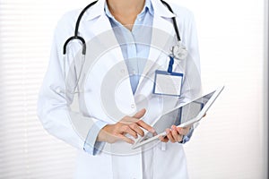 Doctor woman using tablet in clinic office. Unknown female physician at work while standing straight at hospital, close