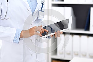 Doctor woman using tablet in clinic office. Unknown female physician at work while standing straight at hospital, close