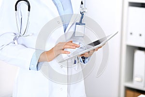 Doctor woman using tablet in clinic office. Unknown female physician at work while standing straight at hospital, close
