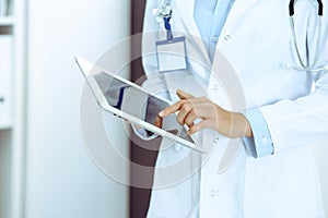 Doctor woman using tablet in clinic office. Unknown female physician at work while standing straight at hospital, close