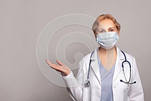 Doctor woman wearing medical uniform over gray background presenting and pointing with palm of hand looking at the camera