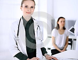 Doctor woman at work with patient and colleague at background. Physician filling up medical documents or prescription