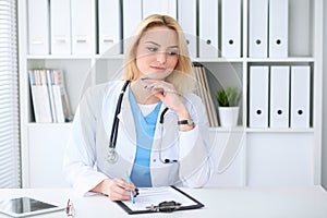 Doctor woman at work. Portrait of cheerful smiling blonde physician sitting at the desk. Medicine and healthcare concept