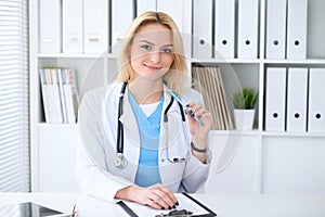 Doctor woman at work. Portrait of cheerful smiling blonde physician sitting at the desk. Medicine and healthcare concept
