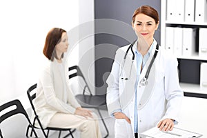 Doctor woman at work. Portrait of female physician cheerful smiling while standing near reception desk at clinic or