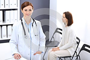 Doctor woman at work. Portrait of female physician cheerful smiling while standing near reception desk at clinic or