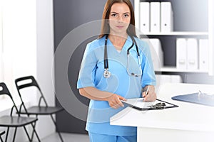 Doctor woman at work. Portrait of female physician filling up medical form while standing near reception desk at clinic