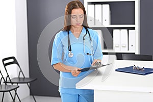 Doctor woman at work. Portrait of female physician filling up medical form while standing near reception desk at clinic