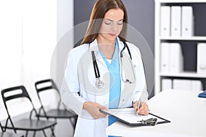 Doctor woman at work. Portrait of female physician filling up medical form while standing near reception desk at clinic