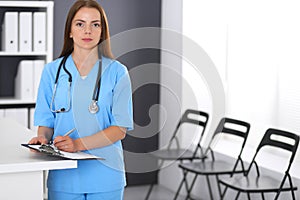 Doctor woman at work. Portrait of female physician filling up medical form while standing near reception desk at clinic