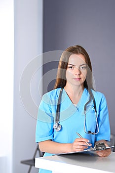 Doctor woman at work. Portrait of female physician filling up medical form while standing near reception desk at clinic