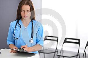 Doctor woman at work. Portrait of female physician filling up medical form while standing near reception desk at clinic