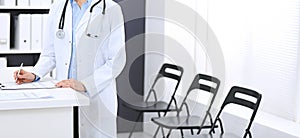 Doctor woman at work. Portrait of female physician filling up medical form while standing near reception desk at clinic