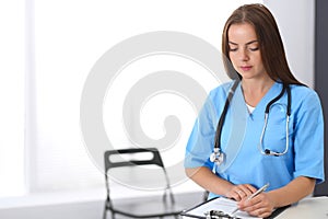 Doctor woman at work. Portrait of female physician filling up medical form while standing near reception desk at clinic